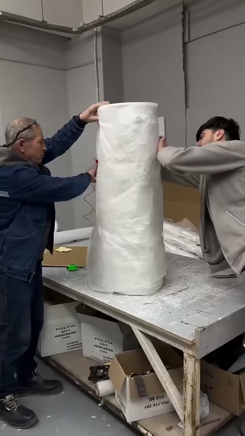 Two workers securing the wrapped column piece in vertical position