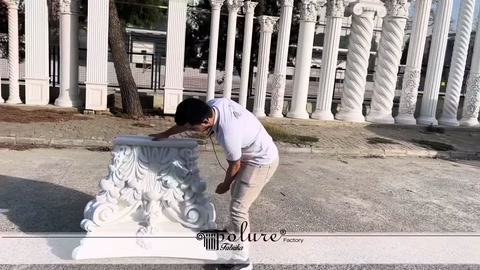 Embossed white column capital being examined by hand in an outdoor space