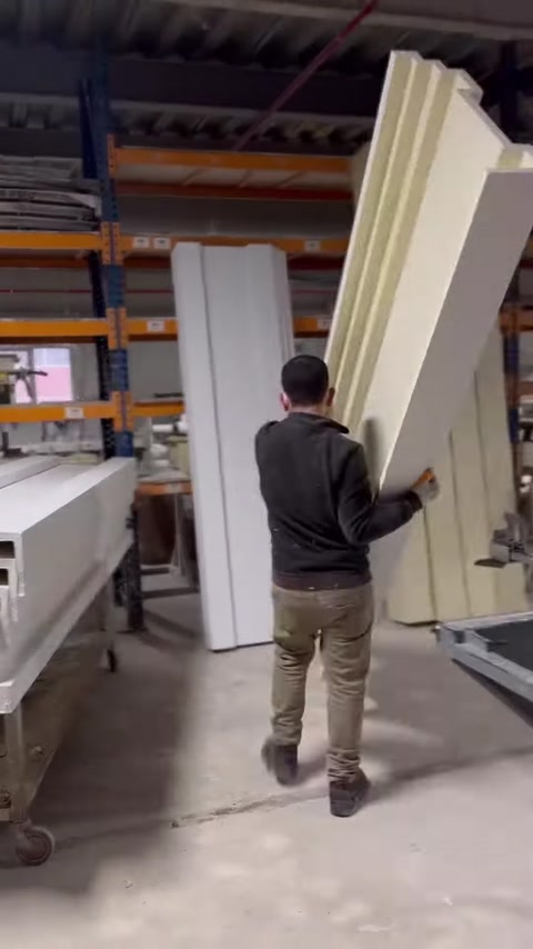 A worker is carrying a long polyurethane profile vertically in the production area.