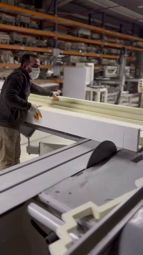 The worker holds the polyurethane cornice on the machine table with both hands.