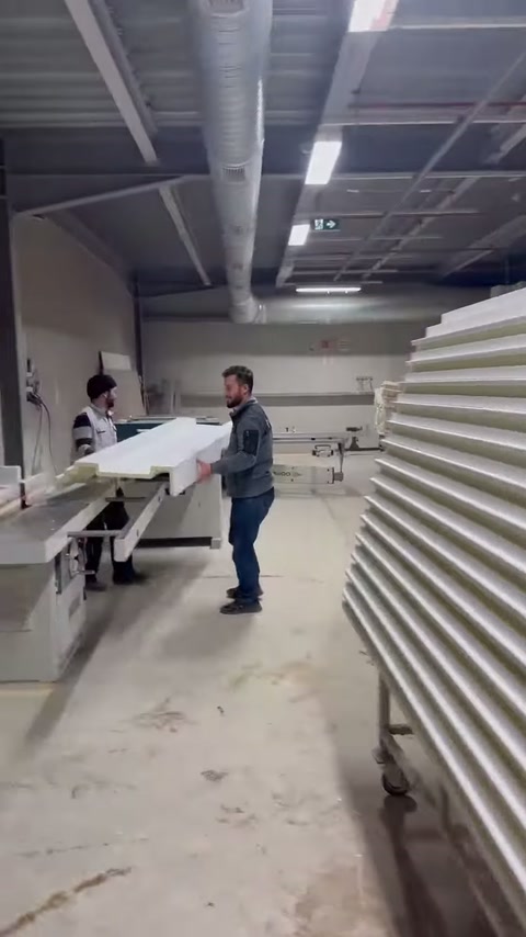 A craftsman is seen carrying a long decorative profile inside the workshop.