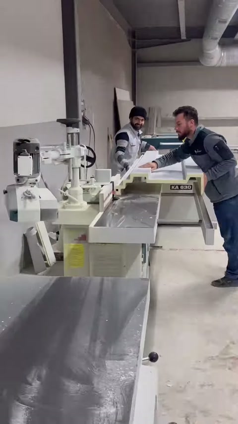 The worker walks toward the machine as cornices are lined up on the right shelf.