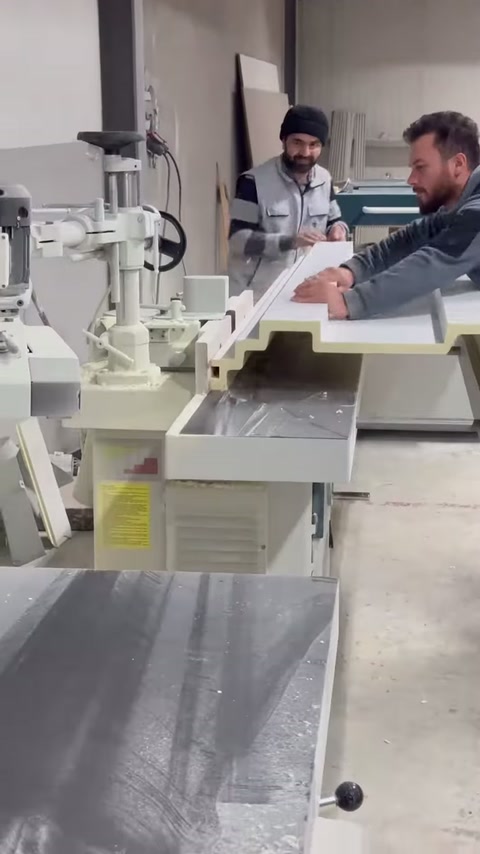 Two craftsmen position the profile piece together on the cutting machine.