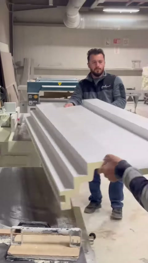 The craftsman works behind stacked long cornices piled on top of each other.