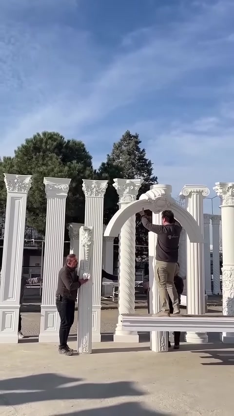 Workers place a curved decorative arch on top of two columns