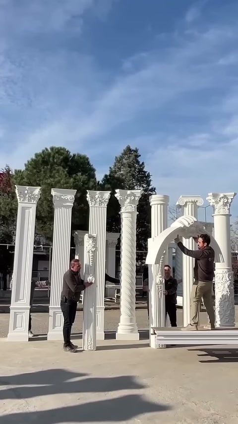 Workers begin to lift a decorative arch piece between the columns