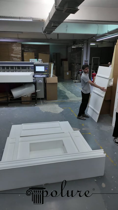 Due operai in laboratorio regolano la posizione del lungo pannello laterale bianco.
