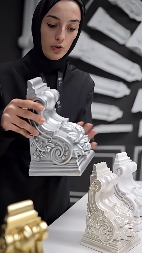 A silver-painted corbel model with raised details is examined in close-up