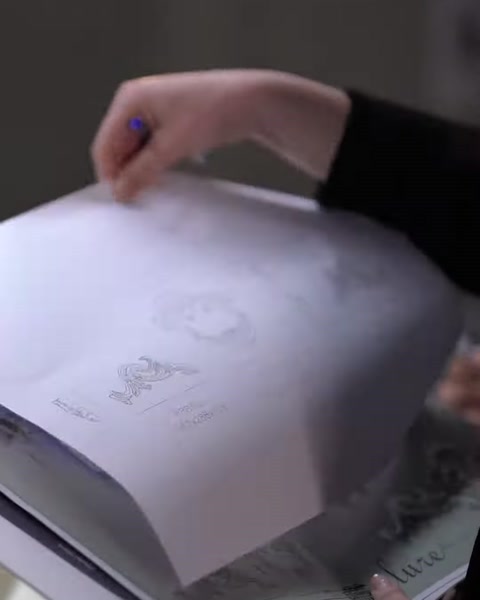 Hand opening a printed project catalog with architectural sketches