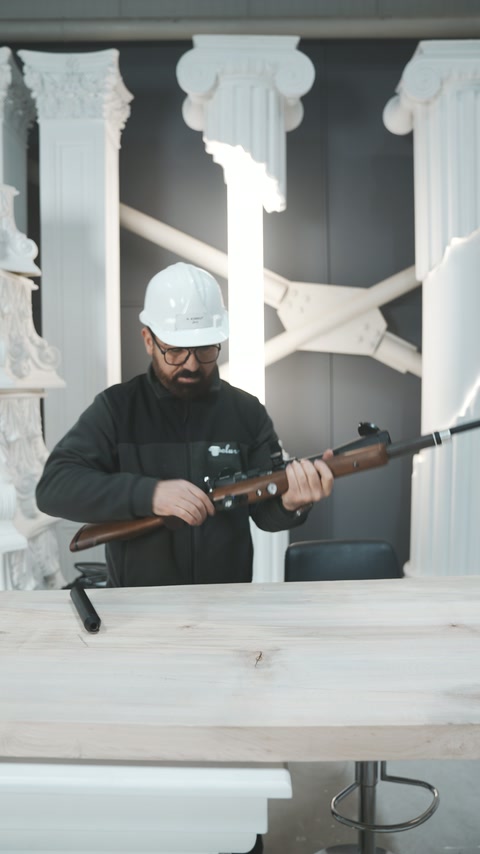 Baretli uygulayıcı dekoratif sütunlar arasında tüfeğin mekanizmasını kontrol ediyor.