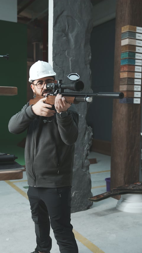 Baretli uygulayıcı atölyede tüfeği karşıya doğrultarak ayakta duruyor.