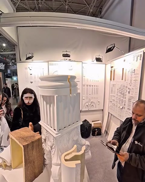 Una donna esamina un pannello di profili per modanature fissato alla parete espositiva dello stand