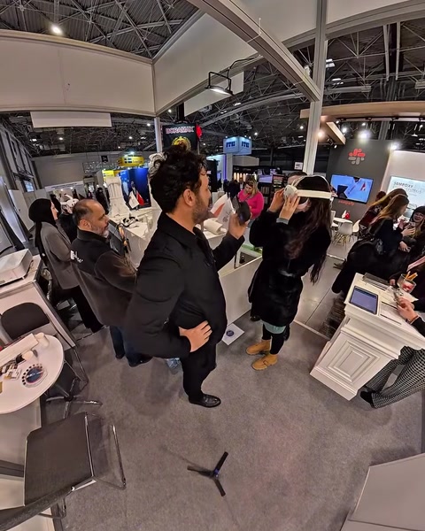 Un uomo con visore per la realtà virtuale gesticola mentre alcune persone osservano un monitor vicino