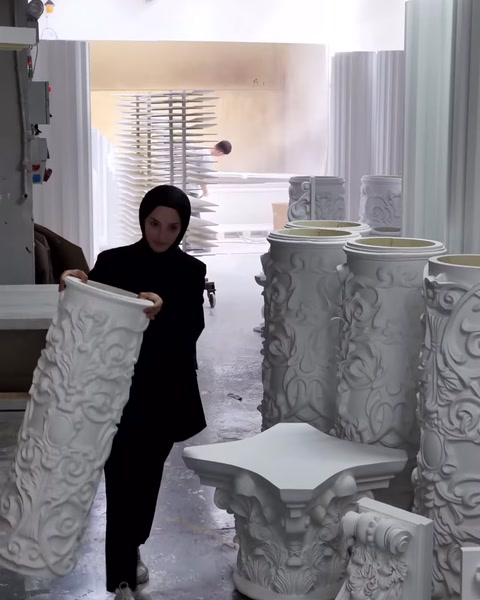 A worker examines an embossed cylindrical column section in the production area.