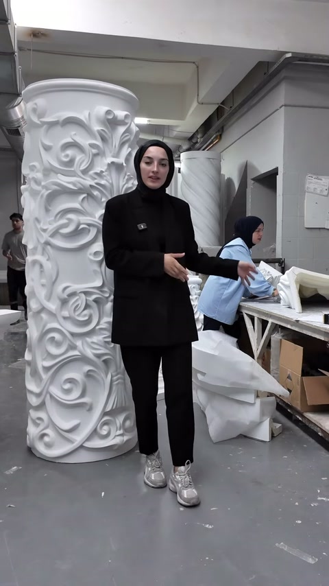 Il presentatore si trova accanto a un fusto di colonna largo con decorazioni vegetali in rilievo nel laboratorio.