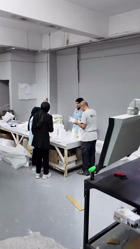 I dipendenti lavorano su pezzi decorativi bianchi al banco mentre il presentatore esamina il processo.
