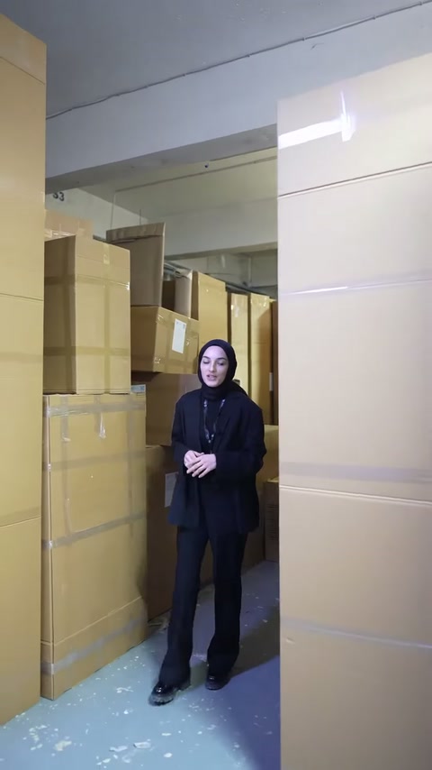 Sunucu, karton kutularla dolu üretim deposunda ilerleyerek bilgi veriyor.