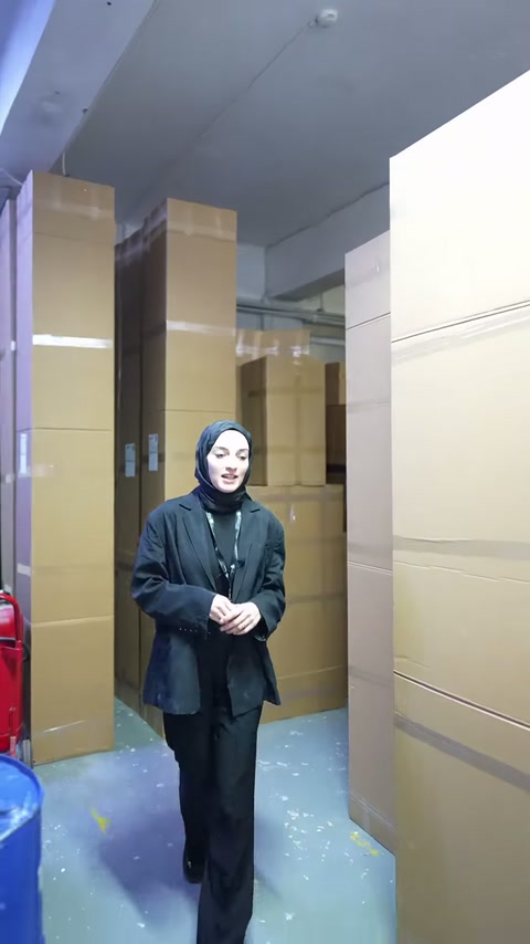 Sunucu, kolilerin dizildiği koridorda üretim alanına doğru yürüyor.