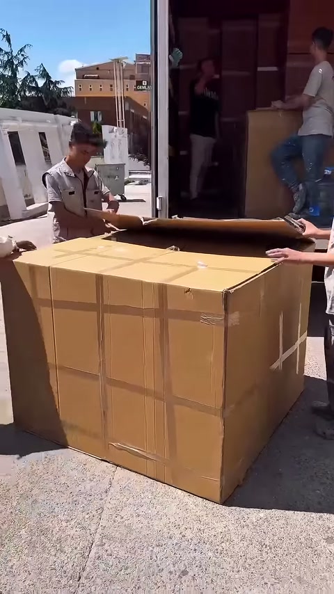 Il largo coperchio superiore dello scatolone di cartone viene aperto da due persone