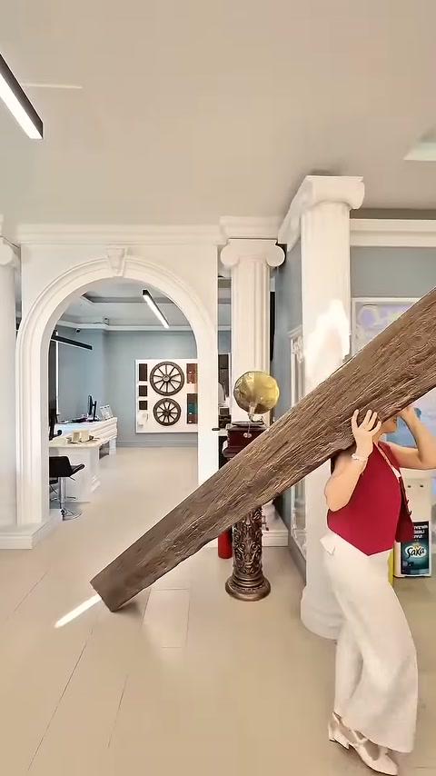 Una lunga trave finto legno viene manovrata oltre le colonne decorative della showroom.
