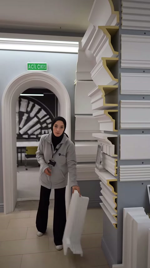 Il presentatore tiene in verticale un lungo profilo bianco per contorno finestra davanti allo scaffale.