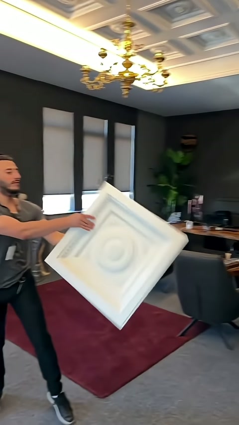 Presenter introduces square ceiling element at an angle in a living room setting.
