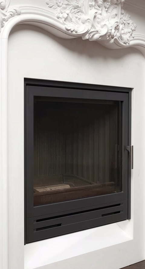 Inserto per camino con vetro nero inserito in una cornice bianca riccamente decorata