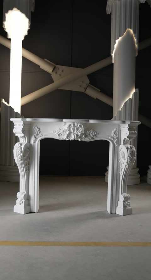 A white ornamental fireplace surround is staged upright inside a workshop.