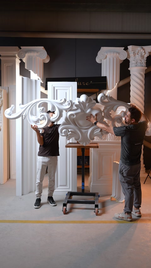 Two workers carefully position an ornate decorative polyurethane element.