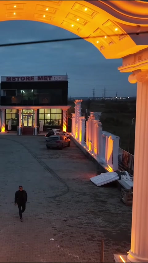 Decorative wall elements and an illuminated entrance gate approaching the building