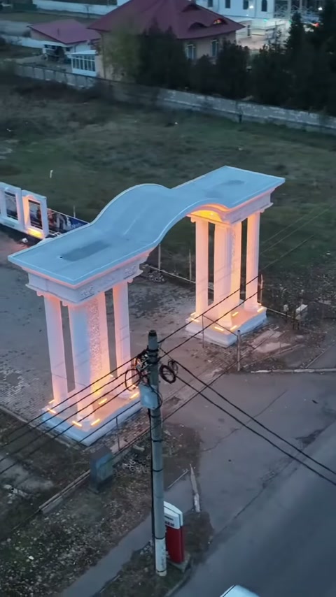 Wavy-topped decorative entrance with illuminated columns visible along the roadside