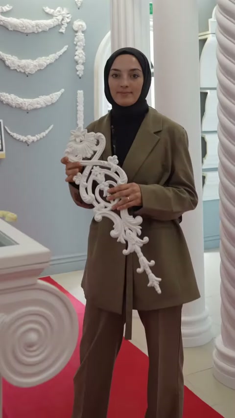 Un addetto espone una grande cornice decorativa bianca con motivi sinuosi in posizione verticale nella sala esposizione