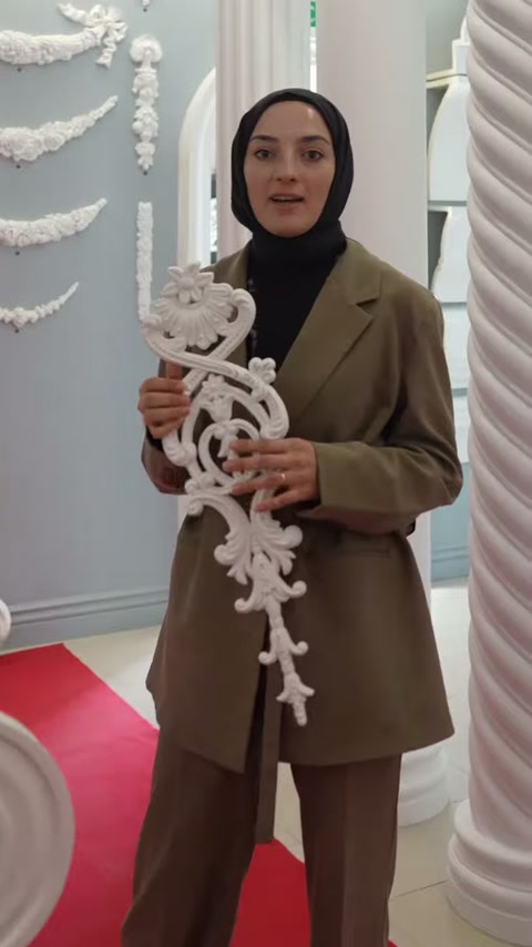 Una cornice decorativa bianca con dettagli elaborati viene presentata a due mani nell'area espositiva tra le colonne
