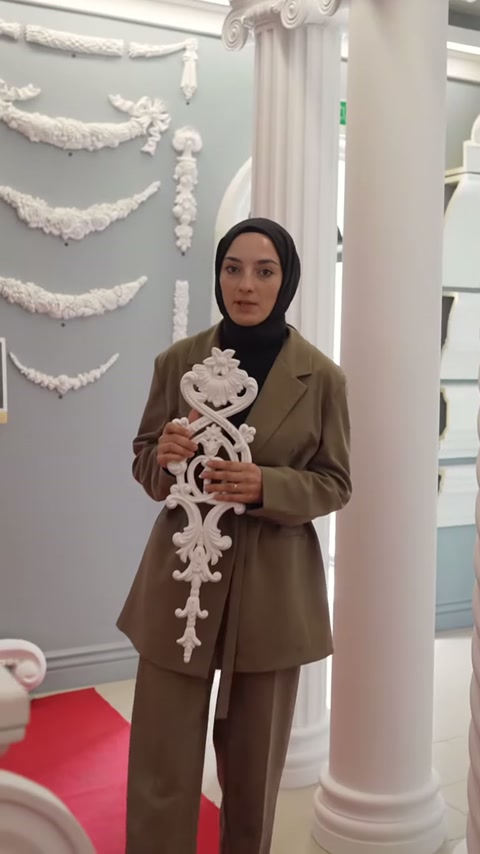 Un motivo decorativo bianco in rilievo viene tenuto a mano accanto a una colonna rosa