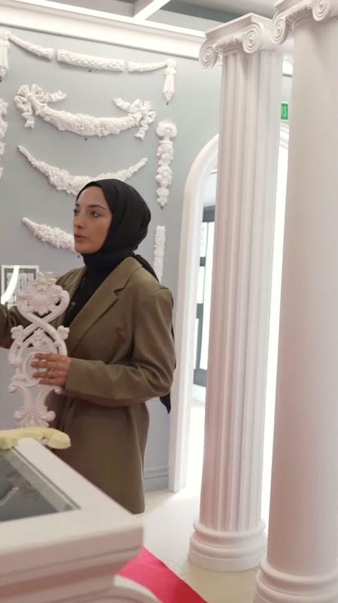 Una cornice bianca in rilievo viene esaminata davanti agli esempi di decorazioni murali