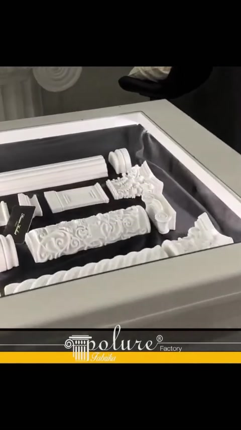 Campioni di profili in poliuretano bianco con diversi motivi su un tavolo espositivo illuminato