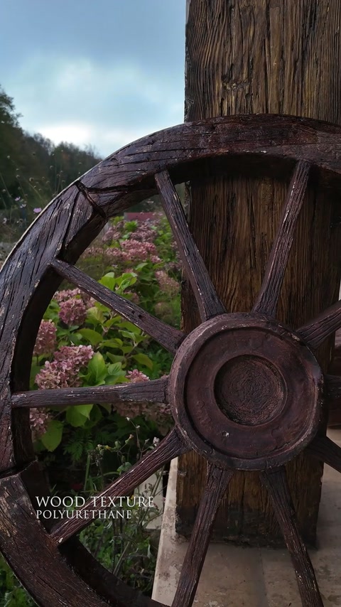 Ruota rustica in poliuretano e colonna effetto legno esposte in un giardino.