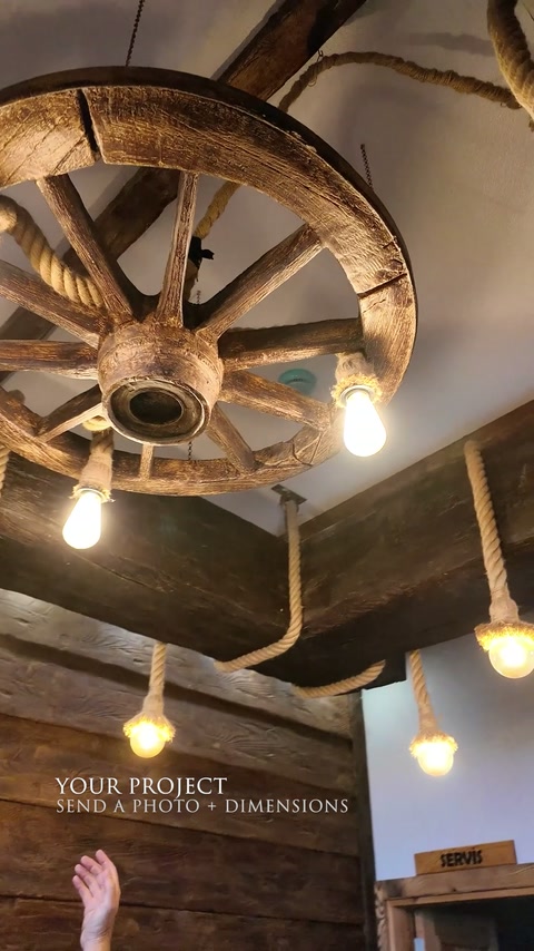 Una lampada a sospensione a forma di ruota di carro completa le travi effetto legno scure in un interno rustico.