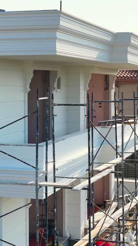 Workers install layered cornices around the upper facade from scaffolding.