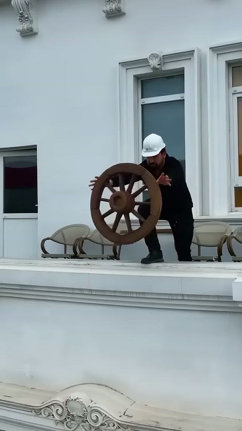 Il maestro sulla terrazza mostra con le mani un elemento decorativo rotondo in stile rustico.