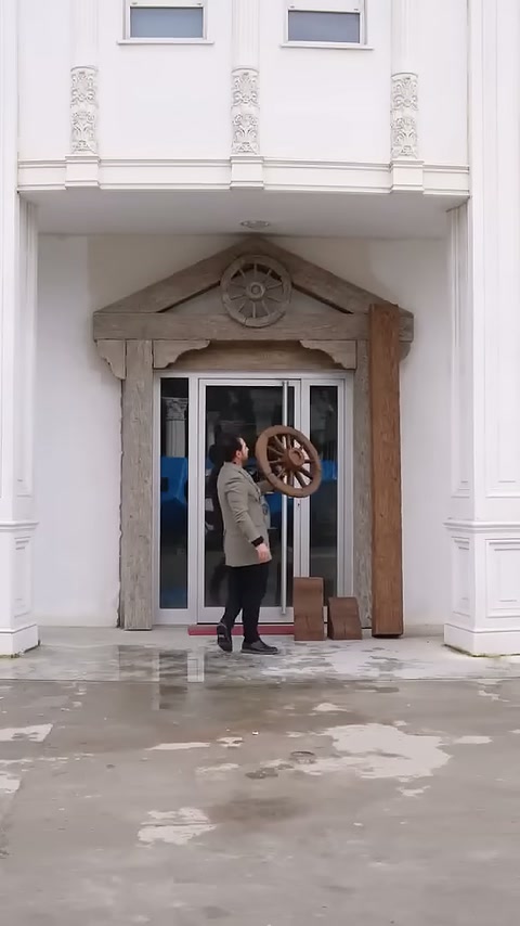 Il maestro davanti alla porta solleva verso l'alto un pezzo decorativo rotondo.