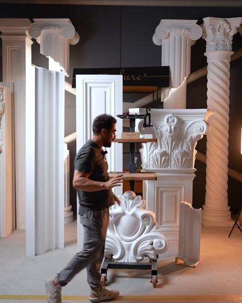 Man carrying floor molding panel past row of Corinthian capitals