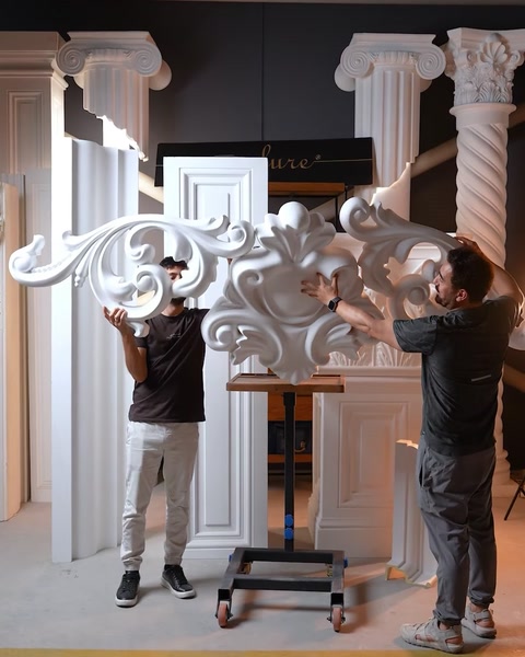 Two men holding large carved openwork scroll appliques for entrance