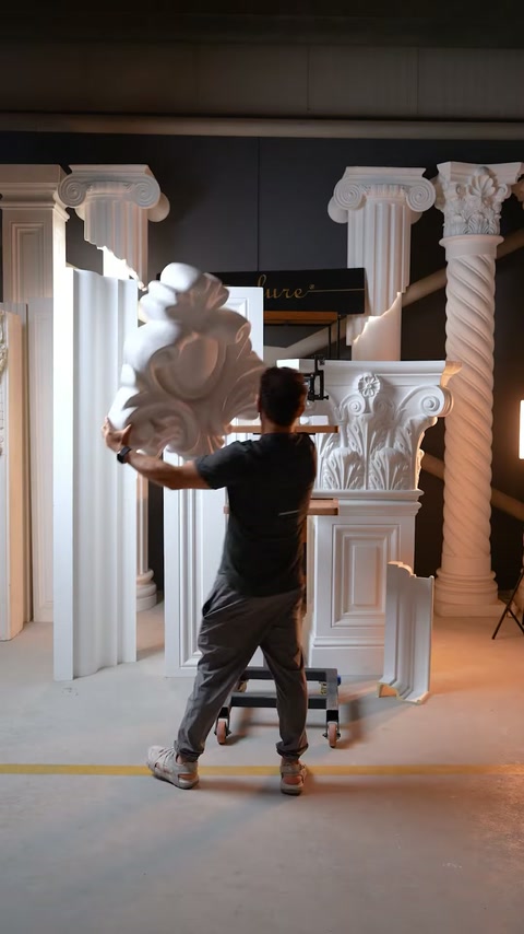 L'operaio solleva un ornamento di voluta intagliato sovradimensionato accanto ai componenti della colonna.