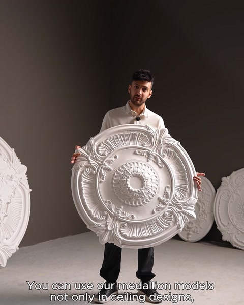 Uomo che tiene in mano un rosone da soffitto bianco rotondo in showroom con modelli impilati
