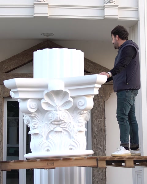 Un operaio su una piattaforma elevata posiziona un capitello sopra un fusto di colonna.