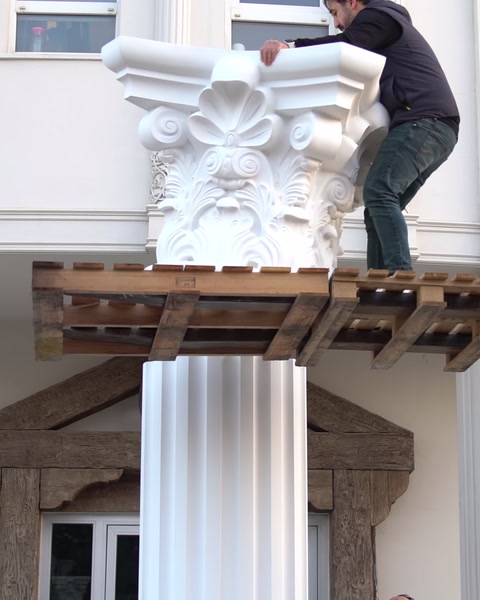 Un operaio cammina su una piattaforma di carrello elevatore accanto a un grande capitello decorativo.