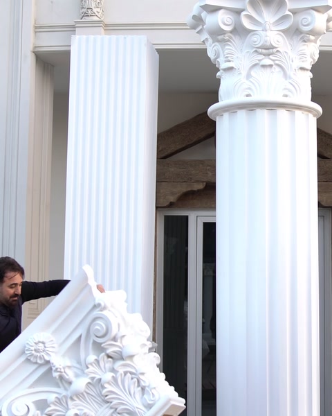 Un operaio abbassa un capitello decorativo su un fusto di colonna già installato.