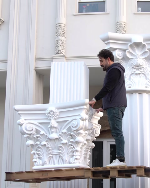 Un operaio su una piattaforma accanto a colonne installate lungo la facciata dell'edificio.