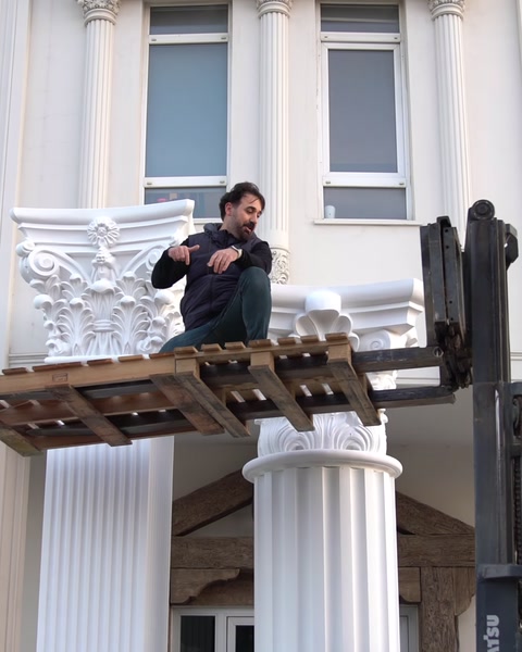 Una piattaforma di carrello elevatore solleva un operaio vicino a una facciata con colonne parzialmente installate.